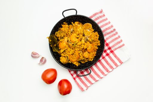 A closeup shot of delicious Spanish rice in a paella pan on a white surface with copy space - great for menu use