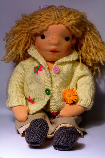 A vertical closeup shot of a handmade fabric doll with blond hair and knitted clothing
