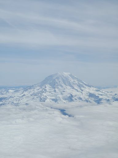 A vertical view of a snowy mountain covered in clouds against a cloudy sky