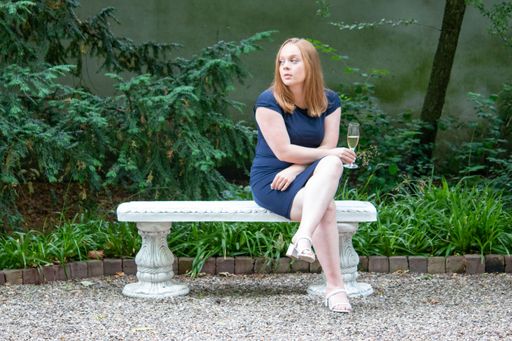 A Caucasian Girl sitting on a bench and looking longingly while holding a drink