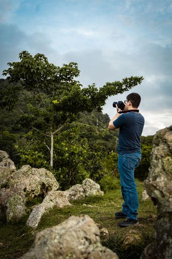 A vertical shot of a Hispanic guy taking photo with a professional camera in a garden