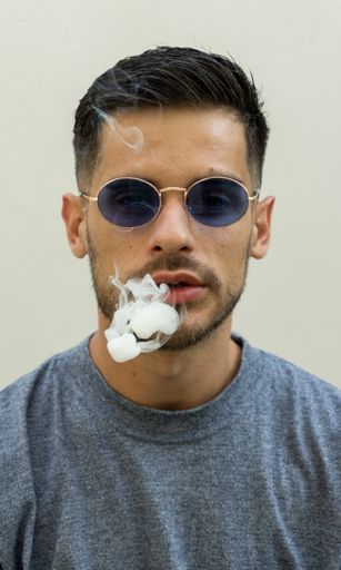 A vertical shot of cigarette smoke getting out of a young caucasian male in sunglasses