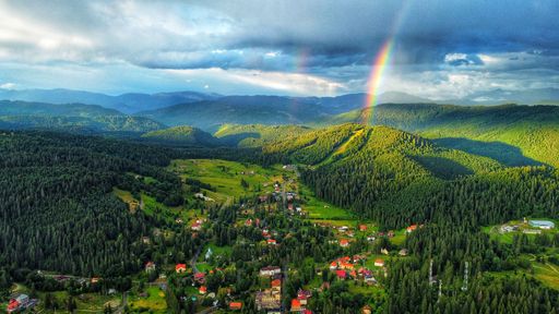 A cityscape view of rainbow cloudy sky over heaven green forest and rural houses