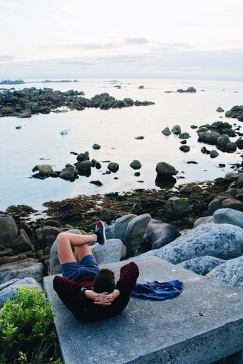 A vertical shot of a male sitting back and relaxing at a rocky beach on a cool day