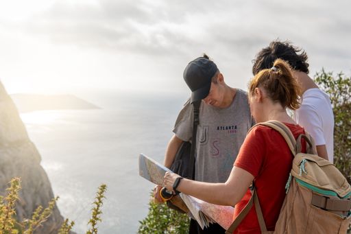 Group of friends with backpacks looking at a map on nature. Freedom, travel and wellness concepts, copy space