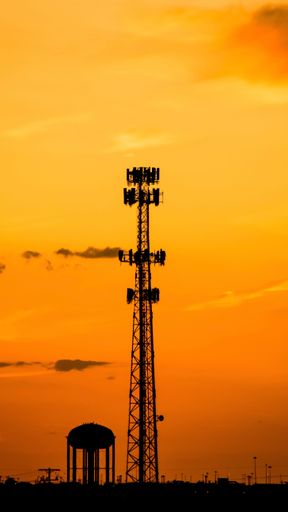 A vertical shot of a silhouette of a transmission tower at a soft orange sunset