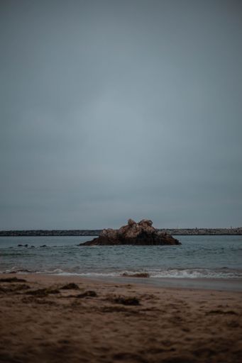 A vertical of ocean waves crashing against rocks on a sandy beach on a gloomy day