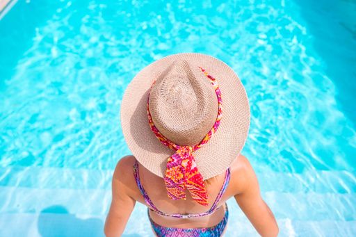A woman in a straw hat at the swimming pool in the summer shot from back - great for a wallpaper