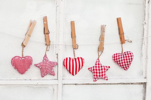 A row of small star and heart-shaped plush toys hanging from a string with clothespins on a white wall