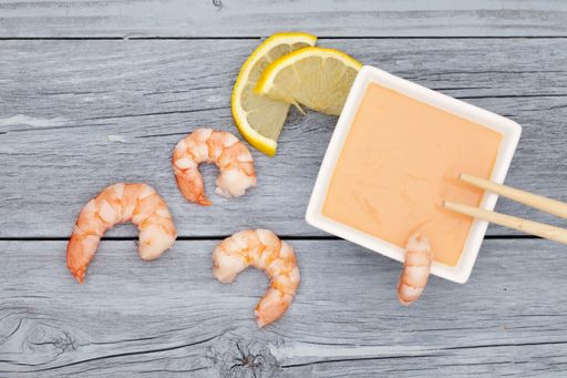A high angle shot of shrimps with lemon and a delicious sauce on a wooden surface