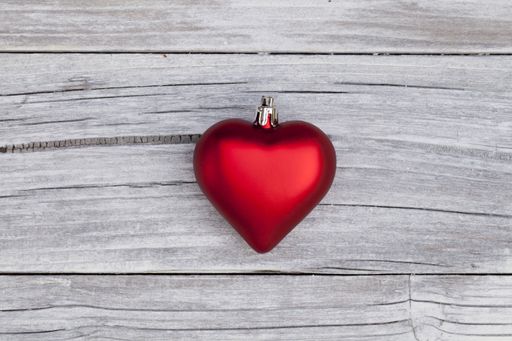 A high angle shot of a red heart-shaped Christmas ornament on a wooden surface