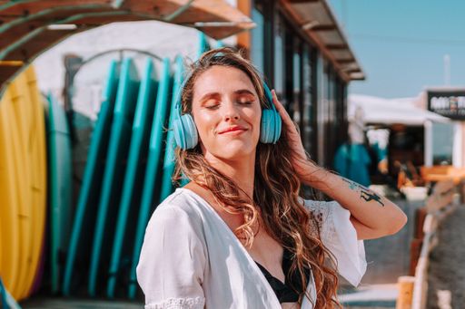 A beautiful woman with blonde wavy hair wearing blue headphones and a beach dress cover up