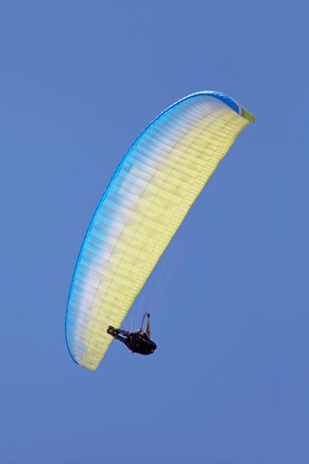 A vertical low angle shot of a person paragliding on a clear blue sky background