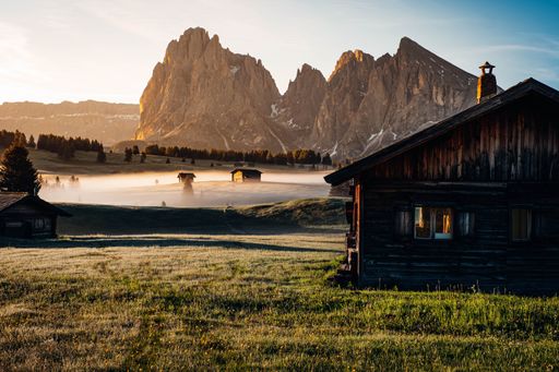 Rural houses and rocky mountains during a foggy sunrise in Seiser Alm, South Tyrol