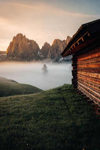 A vertical shot of rural houses and rocky mountains during a foggy sunrise in Seiser Alm, South Tyrol
