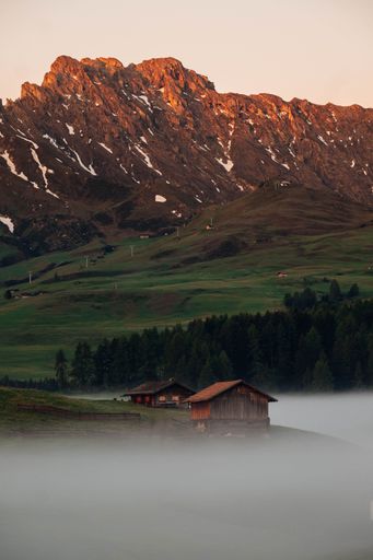 A vertical shot of rural houses and rocky mountains during a foggy sunrise in Seiser Alm, South Tyrol
