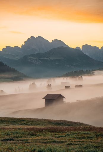 A vertical of a small house in a fog in Seiser Alm meadow, Italy with high mountains in the background