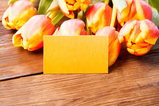 A blank yellow paper and some pink tulips on a wooden surface - empty space for text