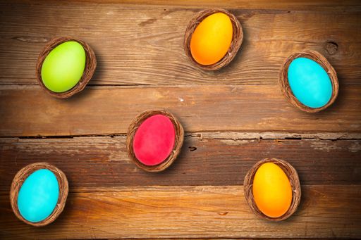 A high angle shot of colorful Easter eggs in bird nests on a wooden surface