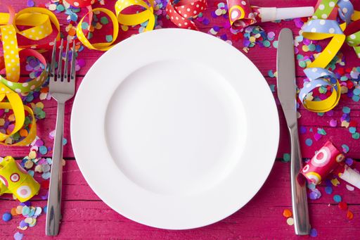 A high angle shot of a plate, fork, and knife on a wooden surface covered with colorful confetti