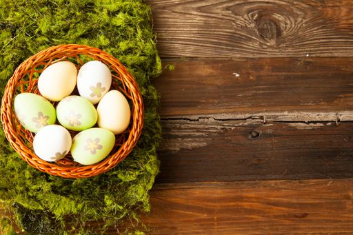 A high angle shot of Easter eggs with painted flowers in a straw basket on a wooden table