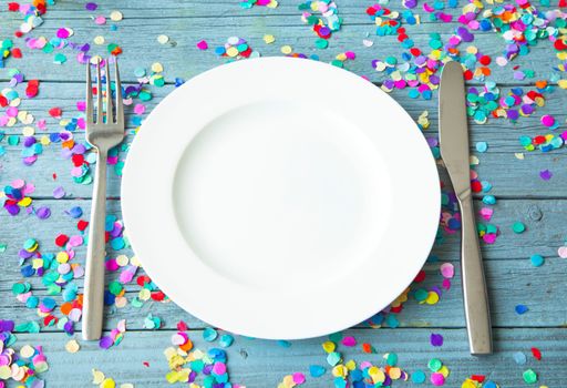 A high angle shot of a plate, fork, and knife on a wooden surface covered with colorful confetti
