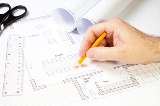 A close up shot of an architect working on a blueprint with a pencil, ruler and scissors