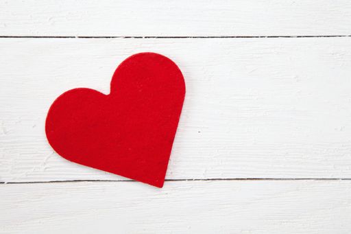 A high angle shot of a red paper heart isolated on a white wooden surface
