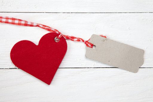 A top view of a heart and a piece of cardboard with space for text tied together on a white wooden surface