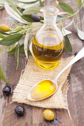 A vertical high angle shot of a bottle and a spoon full of fresh olive oil on a wooden surface