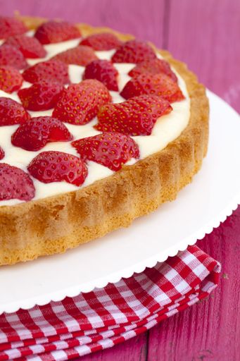 A vertical shot of a delicious strawberry pie in a white plate on a wooden surface