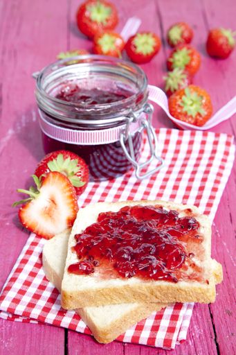 A vertical shot of strawberry jam spread on toasted bread on a decorative pink picnic table