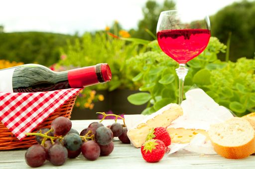 A close up shot of wine, pastry, cheese, grapes and strawberries in a picnic table
