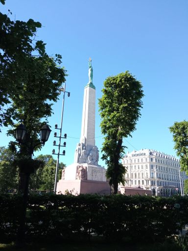 A vertical low angle shot of a statue surrounded by green trees on a sunny day