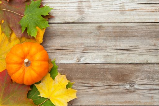 A top view of a pumpkin and colorful leaves on a wooden background with space for text