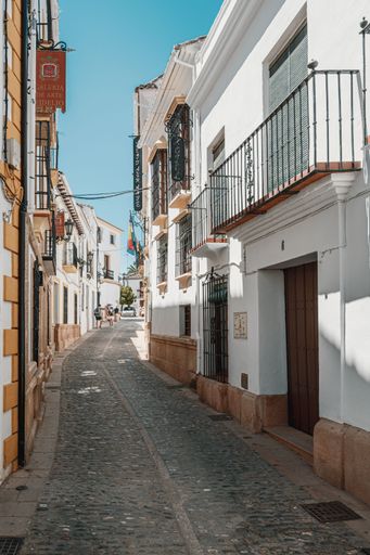 The vertical view of a narrow street with white houses under the blue sky in Ronda