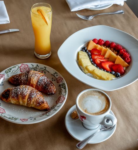 A cup of coffee accompanied by fresh croissants and fruits