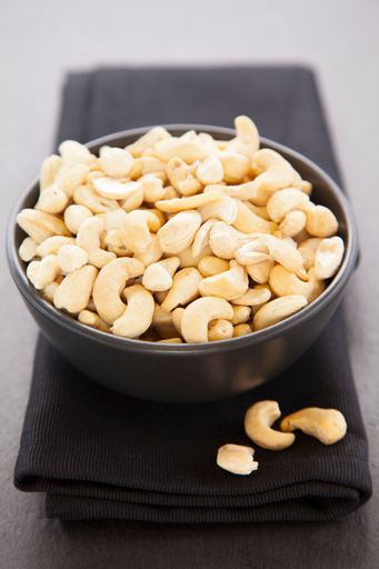 A vertical shot of a black bowl with fresh cashew nuts