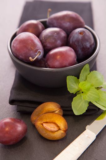 A shallow focus shot of juicy purple plums in a black bowl and on a black surface