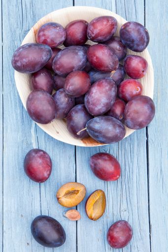 A vertical high angle shot of a plate of fresh plums on a blue wooden surface