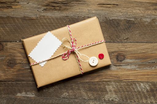 A top view of a gift wrapped with brown paper and red ribbon on a wooden background