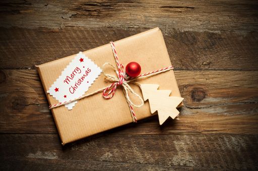 A top view of a wrapped Christmas present with a card that reads Merry Christmas, on a wooden surface