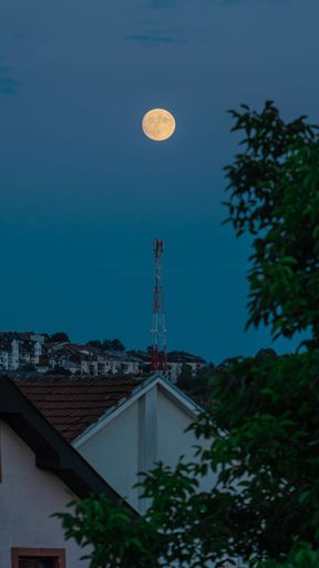 A vertical shot of a full moon above houses in a clear sky