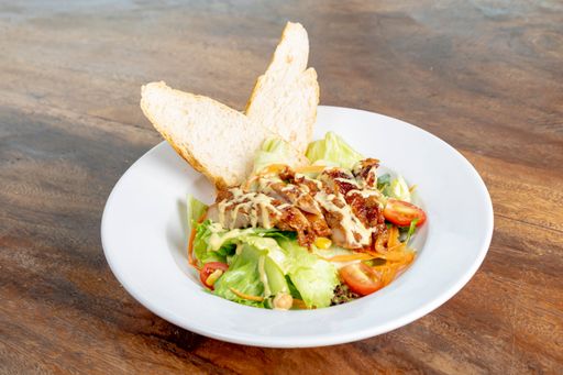 A closeup of a salad with chicken breast, lettuce and carrots served on a white plate