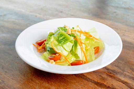 A closeup of a salad with tomatoes, lettuce and carrots served on a white plate