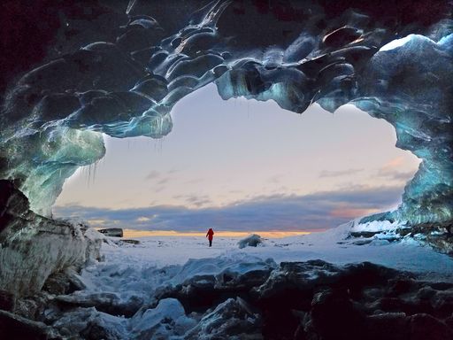 A back view of the female walking towards the golden sunset on a winter day from the frosty cave