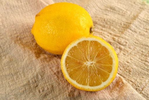An isolated shot of a whole and a sliced lemon on a brown cloth