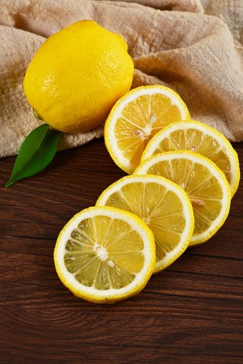 A vertical shot of a whole and slices of lemon on a wooden table