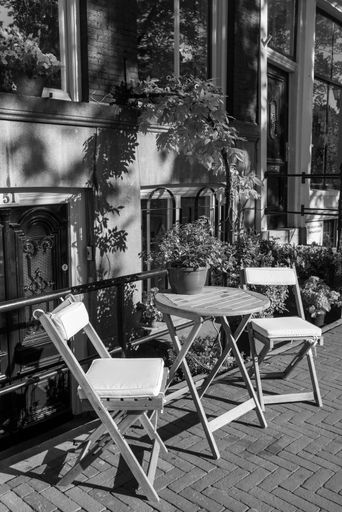 A grayscale vertical view of the table and empty chairs on the sidewalk