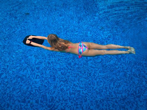 A top view of a young girl in colorful bikini swimming in the pool with black float board